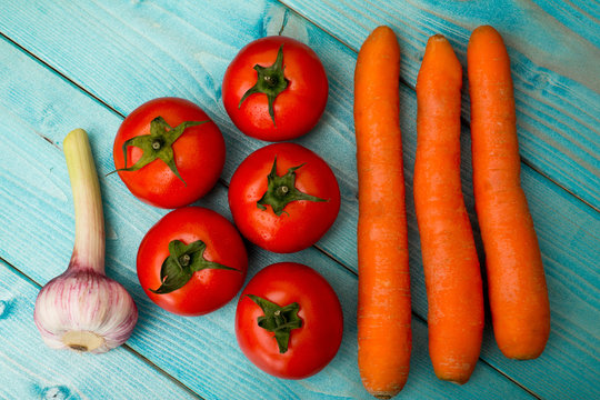 vegetables mix : some raw ripe fresh tomatoes, carrots and garlic over blue table, photo with depth of field