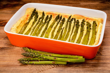 Tart with green asparagus on wooden table.