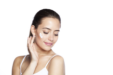 Fototapeta premium Portrait of young woman applying moisturizer cream on her pretty face. Isolated on white background