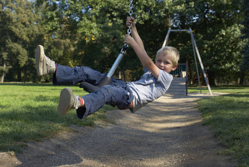 Cute child, boy, rides on Flying Fox play equipment in a children's playground, summertime