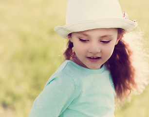Cute kid girl in fashion hat on summer green background with lon