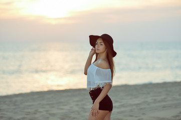 Portrait of beautiful happy woman in hat and shorts enjoying sunset beach background