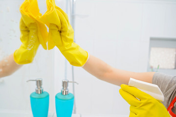 A woman polishing glass using a cleaning sponge and rubber gloves