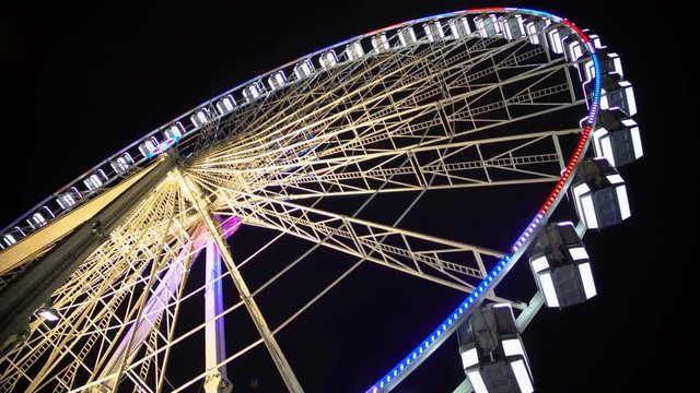 Ferris wheel at amusement park, colorful illuminated construction moving slowly