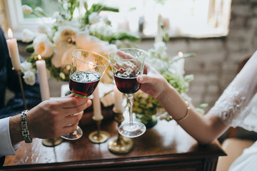 the bride and groom are holding glasses of wine on the background of the composition of candles, flowers, herbs and books on an old wooden table in the loft