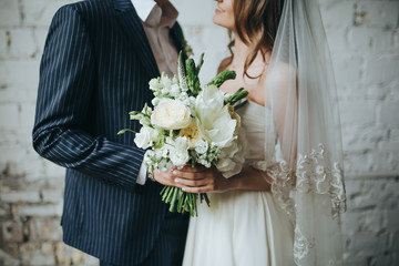 the bride and groom are holding a bouquet of white flowers and greenery in the background Vintage wall of white brick