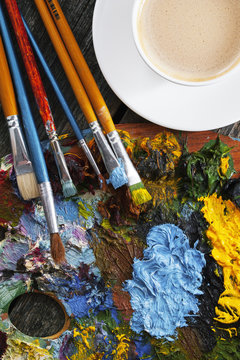 Set of artist brushes, palette, and cup of coffee on wooden background