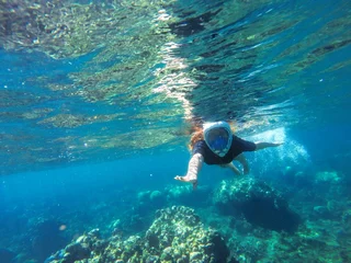 Fotobehang Jonge losse haarvrouw die in blauw masker snorkelt in koraalrif © Elya.Q