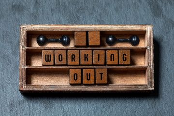 Working out gym concept heading. Aged box, wooden cubes with old style letters, black dumbbells. Gray stone textured background. Close-up, up view