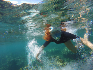 Snorkeling woman making bubbles under water in coral reef
