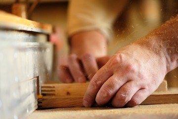 Carpenter's hands cutting piece of wood by cutter