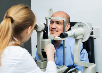 Fototapeta na wymiar Friendly female optician doing eye examination with lamp