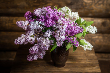 букет сирени из белых и сиреневых цветов на фоне бревенчатых стен в вазе