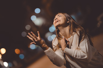 Young emotional stressed woman screaming looking up, city street in the night, evening lights bokeh background outdoors 