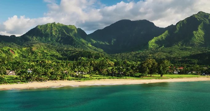 Aerial view flying over tropical blue ocean towards beautiful green mountains and white sandy beach. Hanalei Bay, Kauai