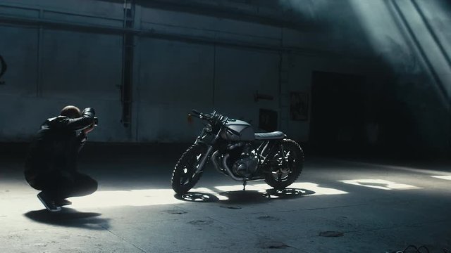 Wide shot of young Caucasian male biker taking photos of his custom built cafe racer motorcycle. 60 FPS slow motion Blackmagic URSA Mini RAW graded footage