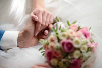 Wedding couple is holding hands. Beauty bride with groom. Beautiful model girl in white dress. Man in suit. Female and male portrait. Close-up woman's arms. Cute lady and guy indoors