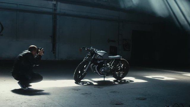 Wide shot of young Caucasian male biker taking photos of his custom built cafe racer motorcycle. 60 FPS slow motion Blackmagic URSA Mini RAW graded footage