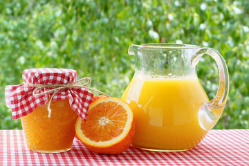 Orange juice, jam, orange halves on a red checkered tablecloth.