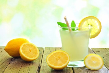 Glass of fresh lemonade on wood with lemons and a defocused outdoor background