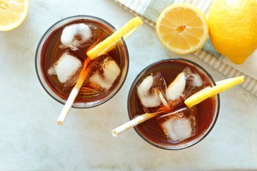 Two glasses of iced tea with lemons, overhead view on a white marble background