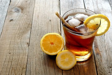 Glass of homemade lemon iced tea with straw on a rustic wooden background