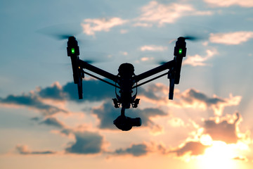 Professional drone with green lights flying at the sunset with dark clouds