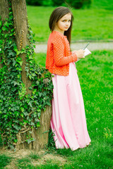 Naklejka premium Girl in dress with notebook and pen near tree