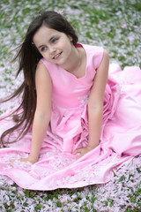 Little girl on green grass with petals