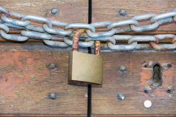 A wooden door locked with a chain and a rusty padlock