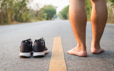 Legs of man with black running shoes on asphalt road in morning