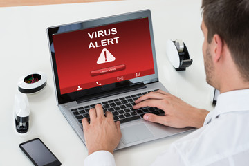 Businessman Using Laptop With Virus Alert On Screen