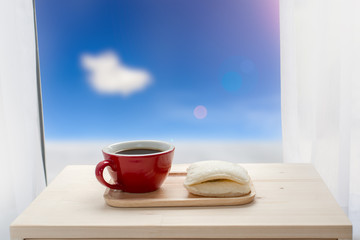 Red coffee cup and sandwich and window facing to snow, blue sky