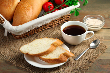 baguettes and vegetables in a wicker basket near the coffee Cup and sliced baguette on a plate with sauce on wooden background