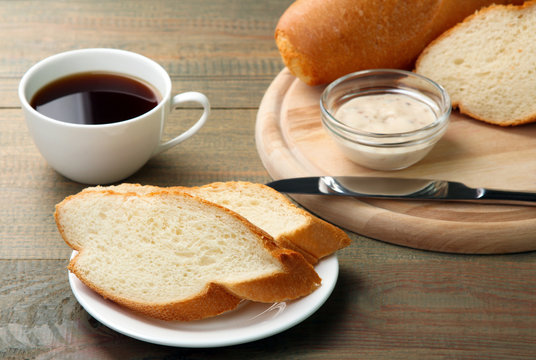 cut the baguette with a knife on wooden cutting Board on wooden background with sauce and a Cup of strong coffee
