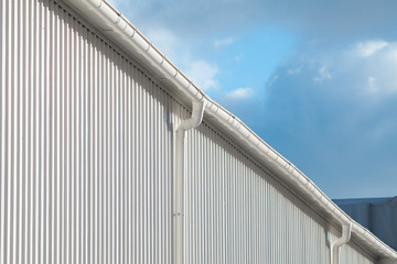 Fototapeta premium New white rain gutter on a building with white metal sheet against blue sky
