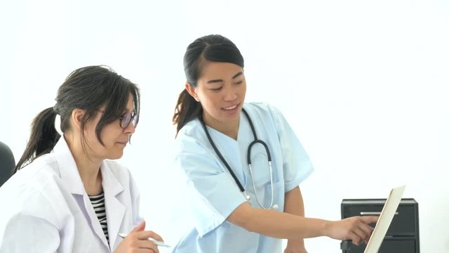 Female mature doctor and medical assistant working together at computer