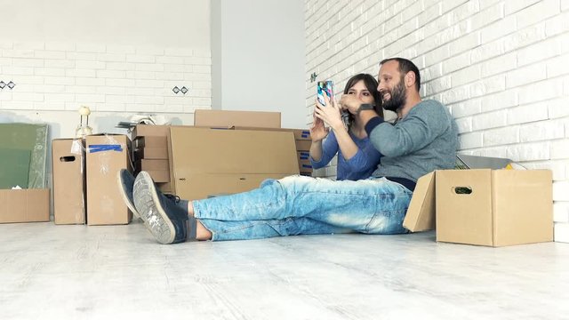 Happy couple with key to their ne home taking selfie photo with cellphone on floor
