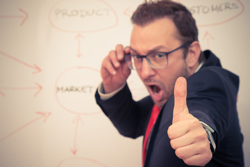 Cheerful businessman with thumbs up gesture in front of the white board with flowchart. Selective focus. Business success concept. 