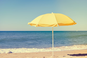 Yellow parasol on desert ocean beach over blue sky