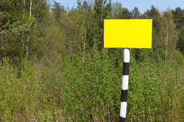 Empty yellow sign board on striped post