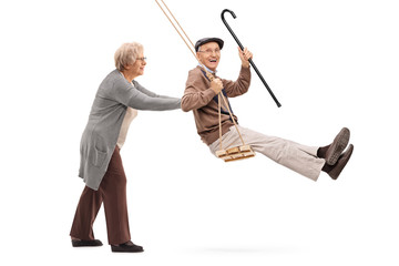 Elderly woman pushing a man on swing - obrazy, fototapety, plakaty