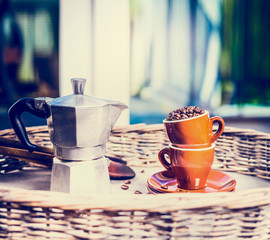 Coffee cups and pot full coffee beans on garden or terrace table over nature background. Morning home scene