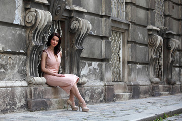 Fototapeta na wymiar Elegant young woman with summer dress and high heels sitting in the window of a palace