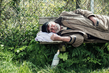 Homeless man sleeping on bench in park.