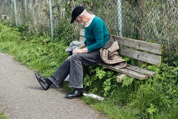 Obraz premium Homeless man gathering stuff on outdoor bench.