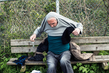 Homeless man on outdoors bench pulling sweater.