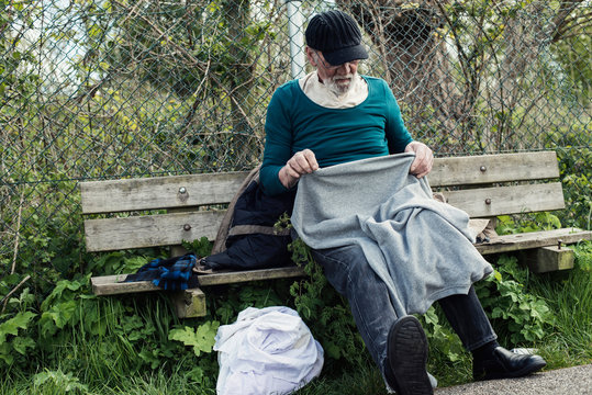 Homeless man on outdoors bench pulling sweater.