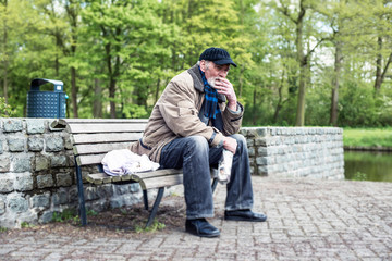Smoking homeless man sitting on bench in park.
