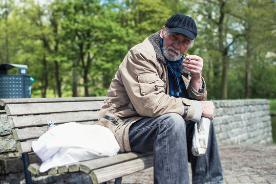 Homeless man smoking cigarette on bench in park.